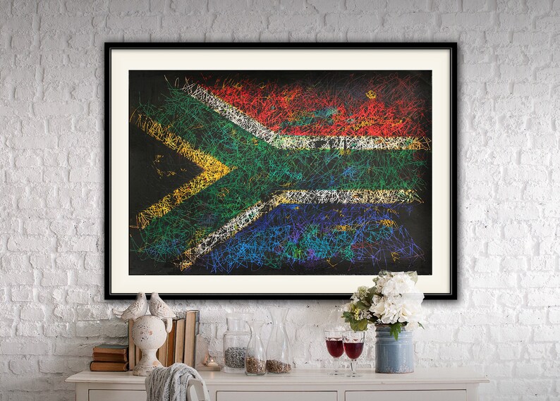 May include: Framed artwork featuring the South African flag, rendered with colorful, textured lines against a black background. The flag's design includes red, white, green, yellow, blue, and black. The artwork is displayed above a white cabinet with decorative items.