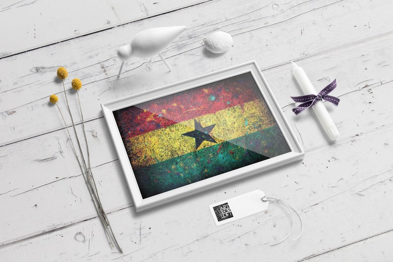 Puede incluir: Una impresi&oacute;n enmarcada de la bandera de Ghana, con un aspecto desgastado y texturizado. La bandera es roja, amarilla y verde con una estrella negra en el centro. El marco es blanco y la impresi&oacute;n est&aacute; sobre una superficie de madera blanca.