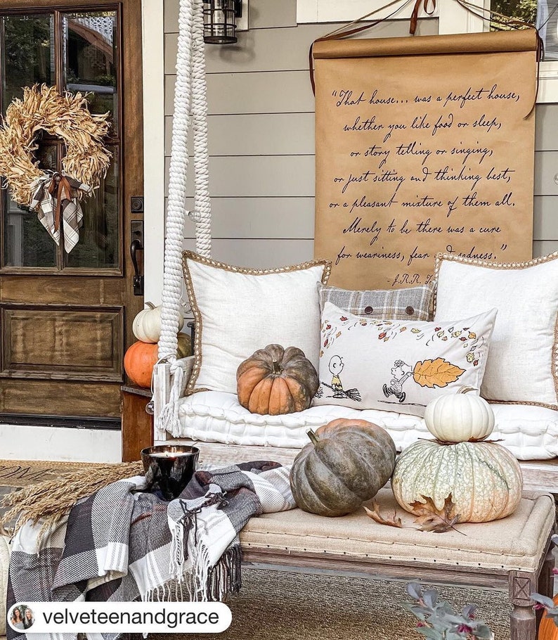 May include: A white porch swing with pillows and pumpkins. The swing is hanging from a wooden beam. A quote about a perfect house is written on a scroll hanging on the wall behind the swing.