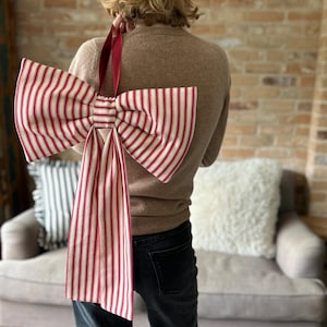 May include: Large decorative bow with red and white vertical stripes. The bow is held by a red ribbon. The bow is made of fabric and is a festive decoration.