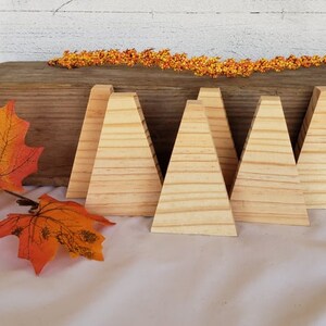 May include: Six unfinished wooden triangular shapes, arranged in a row on a light brown surface. The shapes are made of light wood with a natural grain pattern.