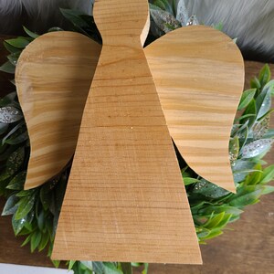 May include: A wooden angel ornament with wings and a simple design. The angel is made of natural wood and has a light brown color.