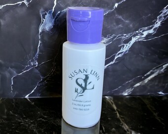 May include: A white plastic bottle with a purple flip top lid. The bottle is labeled "Susan Linn" with a stylized "SL" logo and the text "Lavender Lotion 2 oz/56.9 grams 440-796-5216".