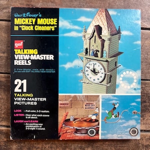 May include: Vintage Mickey Mouse "Clock Cleaners" View-Master reel set. The box features a colourful image of a clock tower and cartoon characters. The set includes 21 talking view-master pictures with 3-D realism.