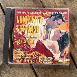 May include: A CD case featuring the movie "Gone With The Wind." The cover art depicts Clark Gable and Vivien Leigh. The text includes "The New Recording of Max Steiner's Classic" and the names of the stars. The CD case is in a clear plastic case.