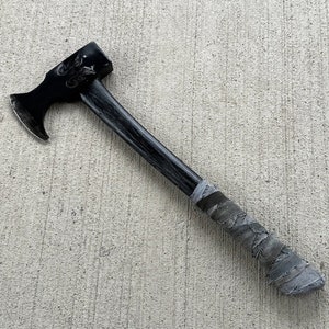 May include: A black axe with a gray fabric handle. The axe head has a decorative design.
