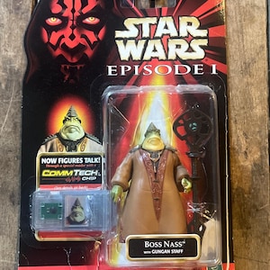 Könnte beinhalten: Star Wars Episode I Boss Nass Actionfigur in Originalverpackung. Die Figur befindet sich in einer transparenten Kunststoffhülle, mit einem braunen und beigen Outfit und einem Stab. Die Verpackung zeigt Darth Maul und den Text "NOW FIGURES TALK!"