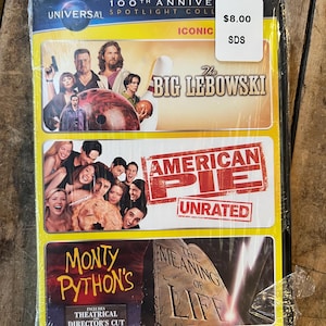 May include: A DVD set containing "The Big Lebowski," "American Pie (Unrated)," and "Monty Python's The Meaning of Life." The packaging is yellow and black, with film stills. The set is sealed in plastic, with a price tag.