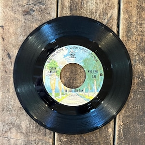 May include: A black vinyl record with a colorful label featuring the text "DA DOO RON RON" by Shaun Cassidy. The label also includes the Warner Bros. Records logo and the text "BURBANK, HOME OF WARNER BROS. RECORDS".