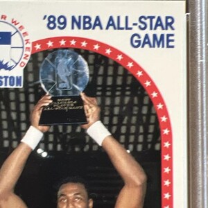 Pu&ograve; includere: Un giocatore di basket alza un trofeo con una base argentata e una parte superiore in vetro trasparente. Il trofeo reca la scritta "NBA All-Star Game". Il giocatore indossa una maglia bianca con un design rosso e blu. Lo sfondo &egrave; un motivo a scacchi bianco e nero.