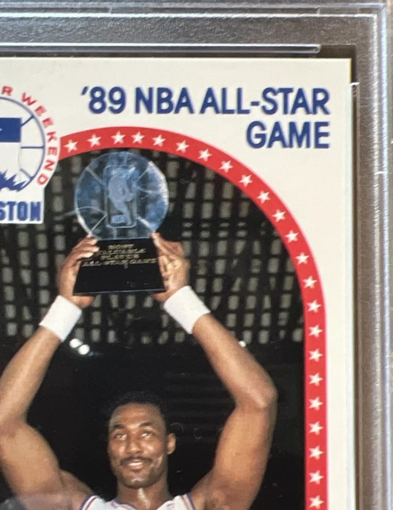 Pu&ograve; includere: Un giocatore di basket alza un trofeo con una base argentata e una parte superiore in vetro trasparente. Il trofeo reca la scritta "NBA All-Star Game". Il giocatore indossa una maglia bianca con un design rosso e blu. Lo sfondo &egrave; un motivo a scacchi bianco e nero.