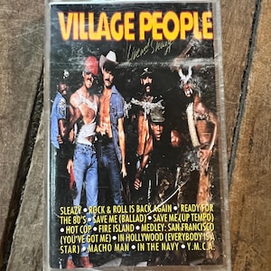 May include: A vintage cassette tape of the Village People's album "Live and Sleazy." The cover features a group of men in various costumes. The tracklist includes songs like "Macho Man" and "Y.M.C.A." The cassette is in a clear plastic case.