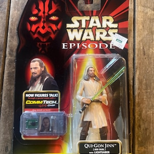 Könnte beinhalten: Star Wars Episode 1 Actionfigur von Qui-Gon Jinn mit Lichtschwert, in Originalverpackung. Die Verpackung zeigt Darth Mauls Gesicht und den Text "Now Figures Talk!" und "COMMTECH CHIP". Die Figur ist für Kinder ab 4 Jahren geeignet.