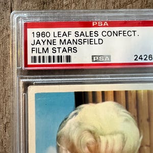 May include: A vintage 1960 Leaf Sales Confection Jayne Mansfield Film Stars trading card in a PSA graded holder. The card features a color photo of Jayne Mansfield with a blonde bouffant hairstyle.