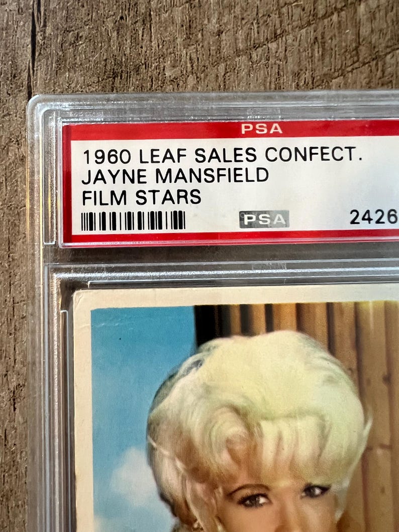 May include: A vintage 1960 Leaf Sales Confection Jayne Mansfield Film Stars trading card in a PSA graded holder. The card features a color photo of Jayne Mansfield with a blonde bouffant hairstyle.