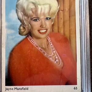 May include: A vintage trading card featuring a portrait of Jayne Mansfield. She is wearing a red sweater and a pearl necklace. The card has a white background with the text "Jayne Mansfield" and "63" printed on it.