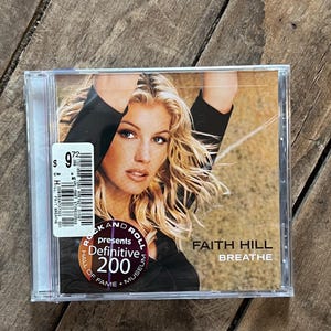 May include: A CD case featuring Faith Hill's album "Breathe." The cover art shows a close-up of Hill with blonde hair. The CD case has a sticker with a price tag. The Rock and Roll Hall of Fame logo is also visible.