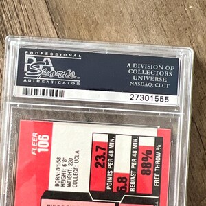 May include: A graded sports trading card in a protective case. The card features a red and white design with player statistics, including points per 48 minutes and free throw percentage. The case is labeled "PSA Sports Authenticator."