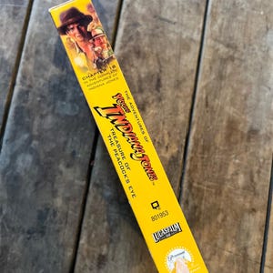 May include: A yellow VHS tape box for "The Adventures of Young Indiana Jones: Treasure of the Peacock's Eye." The box features images of Indiana Jones and the text "Chapter 18" and the Lucasfilm and Paramount logos.