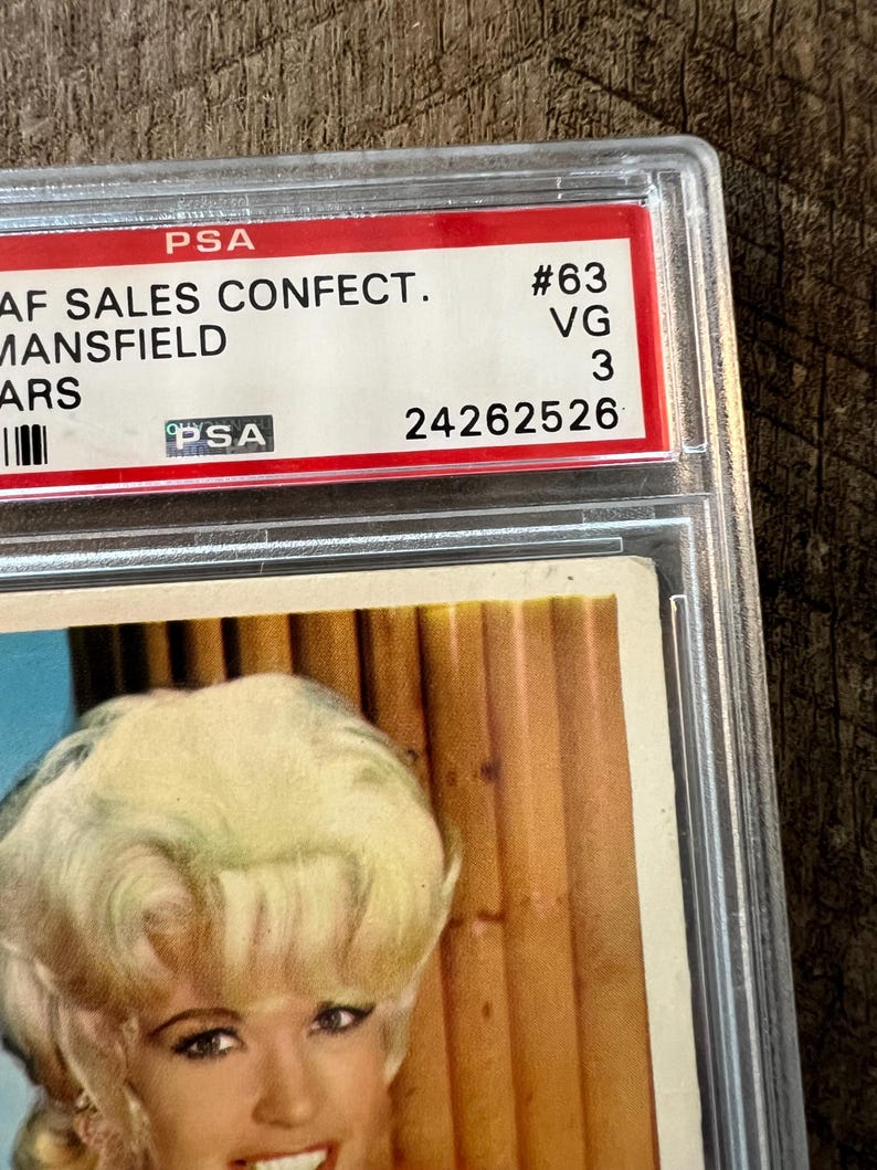 May include: A vintage trading card featuring a woman with blonde hair and a white dress. The card is graded by PSA and has a grade of VG 3. The card number is #63. The text on the card reads "AF SALES CONFECT. MANSFIELD ARS".