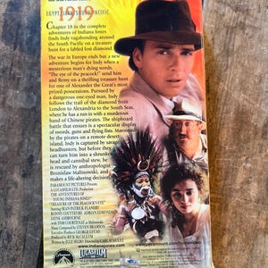 May include: A VHS tape for "The Adventures of Young Indiana Jones: Treasure of the Peacock's Eye." The cover features Sean Patrick Flanery in a fedora, with other cast members and text about the film. The tape is on a wooden surface.