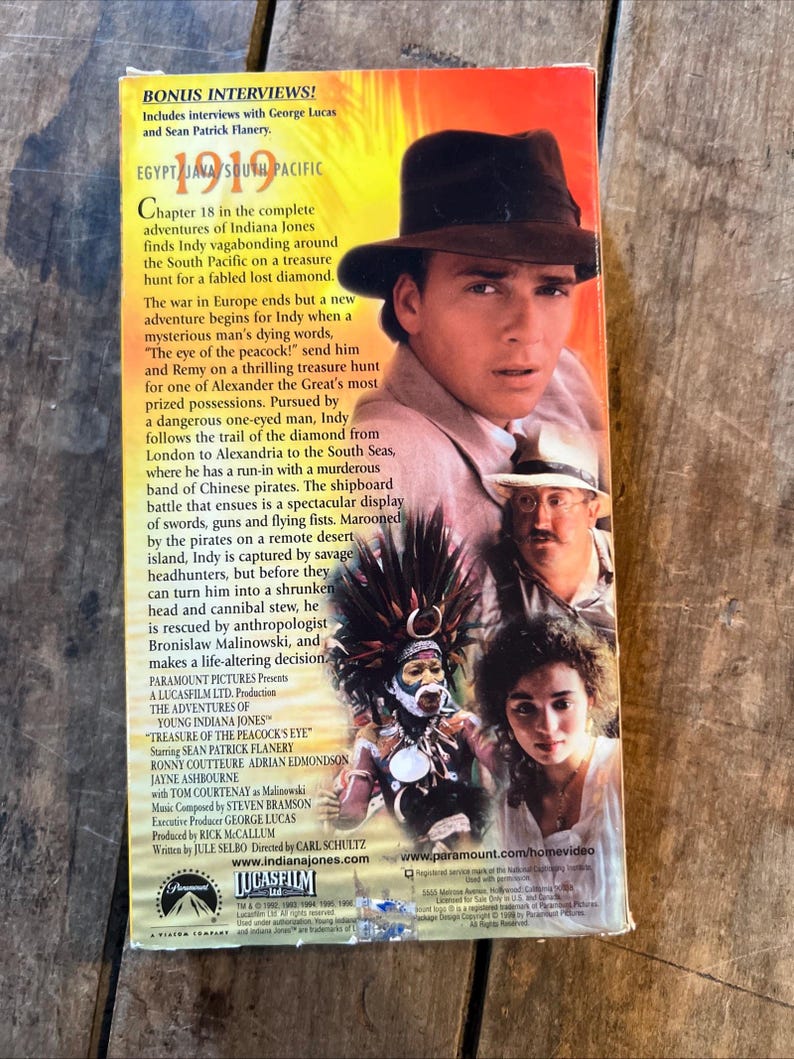 May include: A VHS tape for "The Adventures of Young Indiana Jones: Treasure of the Peacock's Eye." The cover features Sean Patrick Flanery in a fedora, with other cast members and text about the film. The tape is on a wooden surface.