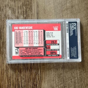 May include: A Kiki Vandeweghe Fleer 106 basketball card, encased in a protective holder. The card features player statistics, including points per game, rebounds, and free throw percentage. The card is from the 1989 Fleer Corp.