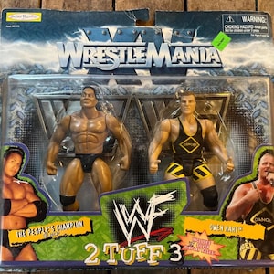 May include: A packaged set of two wrestling action figures from WrestleMania. The figures are in a clear plastic case with the WWF logo and the words "2 Tuff 3". The figures are of The People's Champion and Owen Hart.