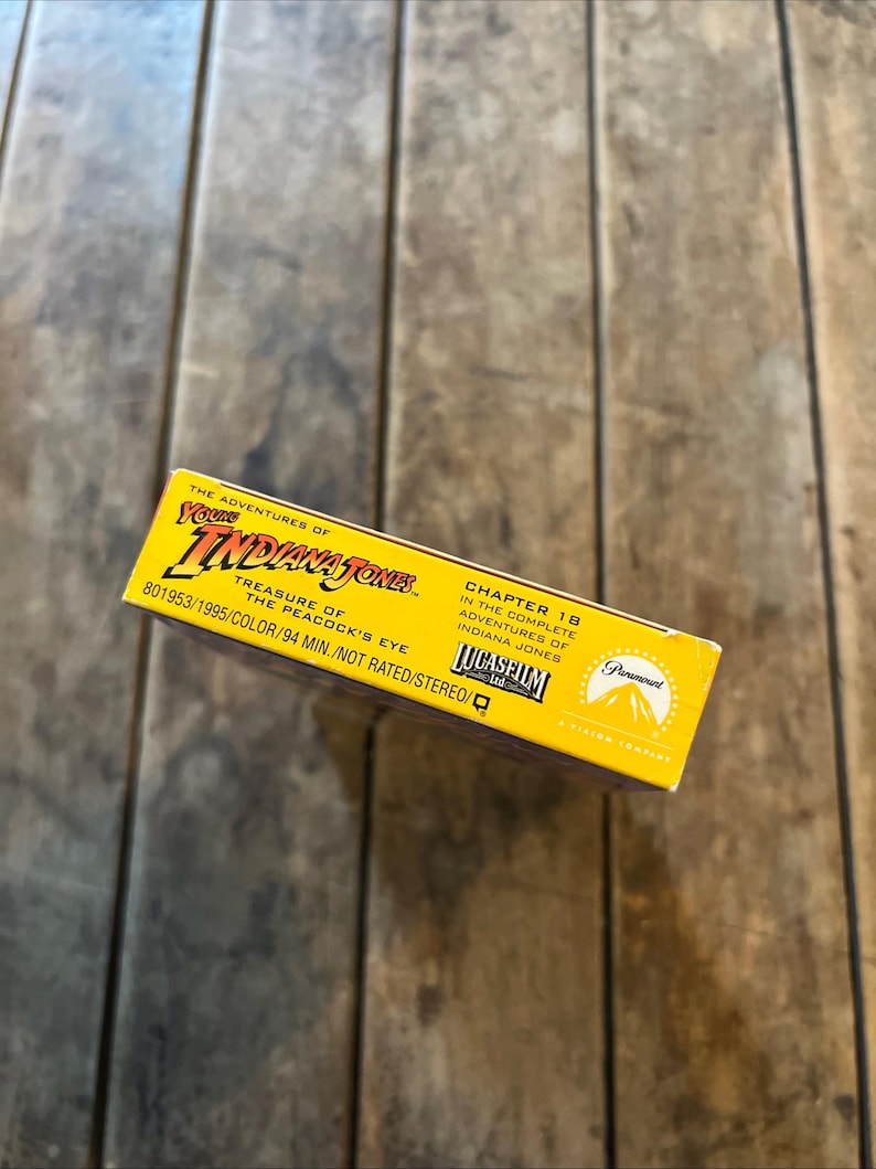 May include: A yellow VHS tape box for "The Adventures of Young Indiana Jones: Treasure of the Peacock's Eye." The box features the Paramount and Lucasfilm logos, with text indicating the chapter number, color, and runtime of 94 minutes.