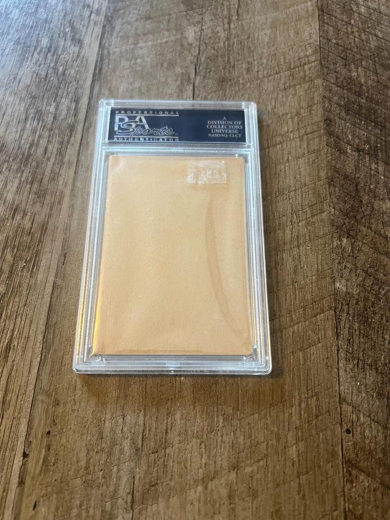 May include: A clear plastic case with a white card inside. The card has a black label with the text "Professional Sports Authenticator, A Division of Collectors Universe,  Sarasota, FL."