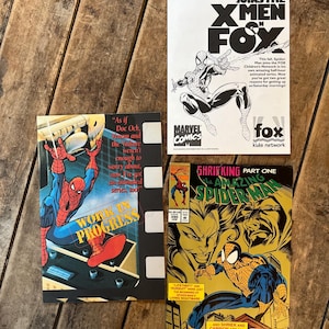May include: Four vintage Spider-Man comic books are displayed on a wooden surface. The comics feature colorful illustrations of Spider-Man in action, with text including "Spider-Man Joins the X-Men" and "The Amazing Spider-Man".