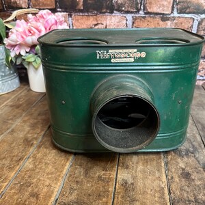 May include: Vintage green metal Mirroscope with a cylindrical lens and two circular openings on top. The word "Mirroscope" is printed on the front. The antique device sits on a wooden surface.
