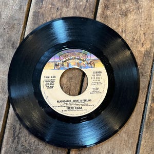 May include: A black vinyl record with the song title "Flashdance... What a Feeling" by Irene Cara. The record label features the Casablanca Records logo and other text. The record is a 45 RPM single.