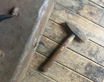 May include: A rusty metal toolbox with a black handle and a small, rusty hammer with a wooden handle. The toolbox and hammer are on a wooden surface.