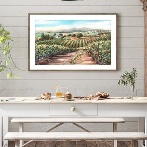 May include: A watercolor painting of a vineyard with a white farmhouse in the distance. The painting is framed in a light wood frame and hangs on a white wall.