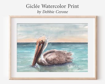 Könnte beinhalten: Ein Giclée-Aquarelldruck von Debbie Cerone, der einen braunen Pelikan zeigt, der in türkisfarbenem Wasser unter einem sanften Horizont schwimmt. Das Kunstwerk ist in einem hellen Holzrahmen gerahmt, mit dem Text Giclée Watercolor Print by Debbie Cerone darüber.