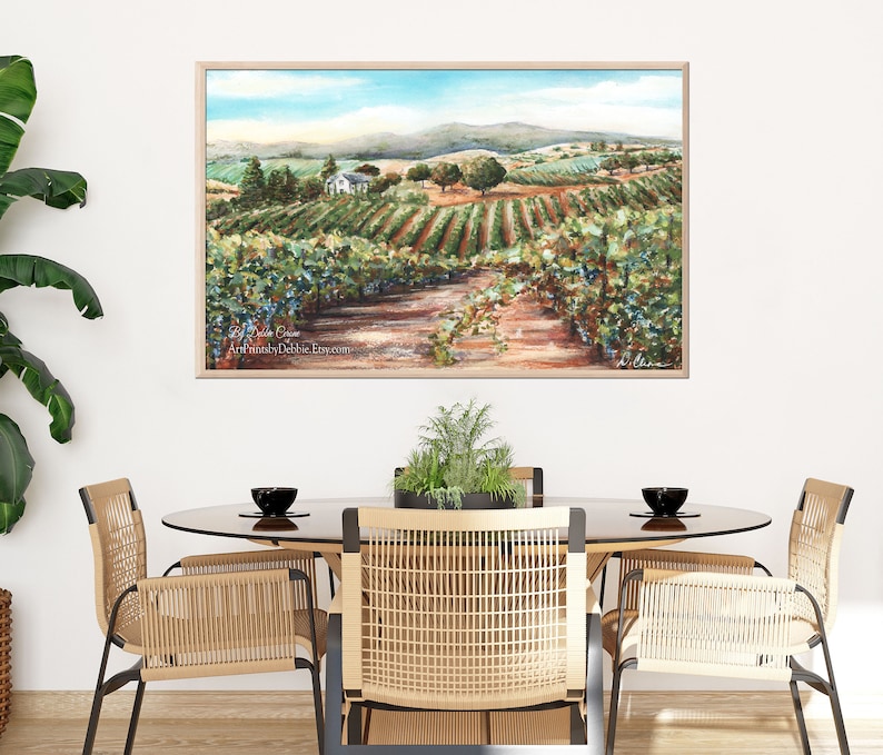 May include: A watercolor painting of a vineyard with rows of grapevines, a small white house, and a dirt path leading through the vineyard. The painting has a blue sky with white clouds and green hills in the background. The text "Debbie Eaton Artist" is in the bottom left corner of the painting.