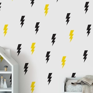 May include: A white wall with a repeating pattern of black and yellow lightning bolts. A white shelf unit with a small house-shaped top is on the left side of the image. A white bench with a grey blanket is on the right side of the image.