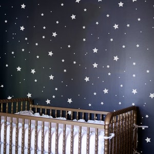 May include: A white crib with a dark blue wall behind it. The wall is decorated with white stars of different sizes.