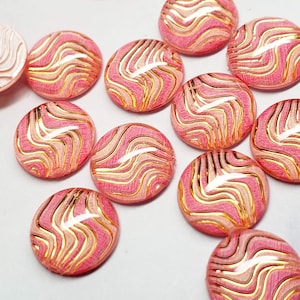 May include: A collection of pink and gold decorative cabochons. Each round cabochon features a swirling pattern of pink, beige, and gold. One cabochon has a textured, wave-like design. These embellishments are ideal for crafting and jewelry making.