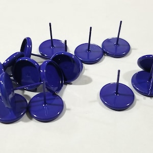 May include: A collection of cobalt blue push pins with a circular head and a straight pin. The pins are scattered across a white surface. The heads of the pins are approximately 1 inch in diameter.