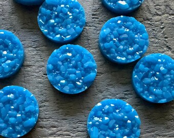May include: A collection of circular, bright blue cabochons featuring a textured, crystalline druzy surface. Each piece has a flat, smooth base and a raised, faceted top that reflects light, creating a sparkling appearance across the set.