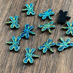 May include: Assortment of 10 blue and green iridescent dragonfly embellishments with glitter accents.