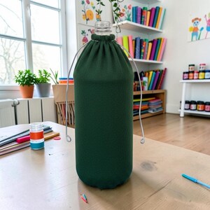 Pu&ograve; includere: Una custodia per bottiglia in tessuto verde scuro con chiusura a coulisse sulla parte superiore. La custodia presenta un sottile manico in filo metallico argentato che parte dal collo della bottiglia e si curva verso il basso su entrambi i lati.