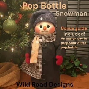 May include: A snowman figurine wearing a dark blue hat with white snowflake patterns, a black and white checkered scarf, and a dark coat with three black buttons. It has red mittens and a tan tag with text. Text reads: Pop Bottle Snowman.