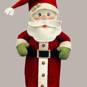 Pu&ograve; includere: Una statuetta di Babbo Natale in peluche con un cappello rosso con pompon bianco, un cappotto rosso con bordo bianco, muffole verdi e una cintura nera con fibbia dorata. Il cappotto presenta una striscia bianca verticale con quattro campanellini.
