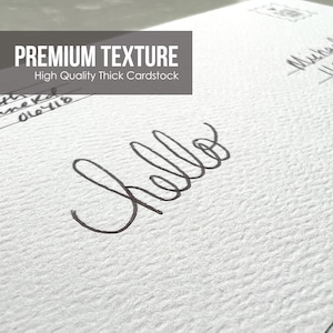 May include: Close-up of a white textured cardstock surface with the word "hello" written in black ink. The text "PREMIUM TEXTURE" and "High Quality Thick Cardstock" is printed at the top of the image.