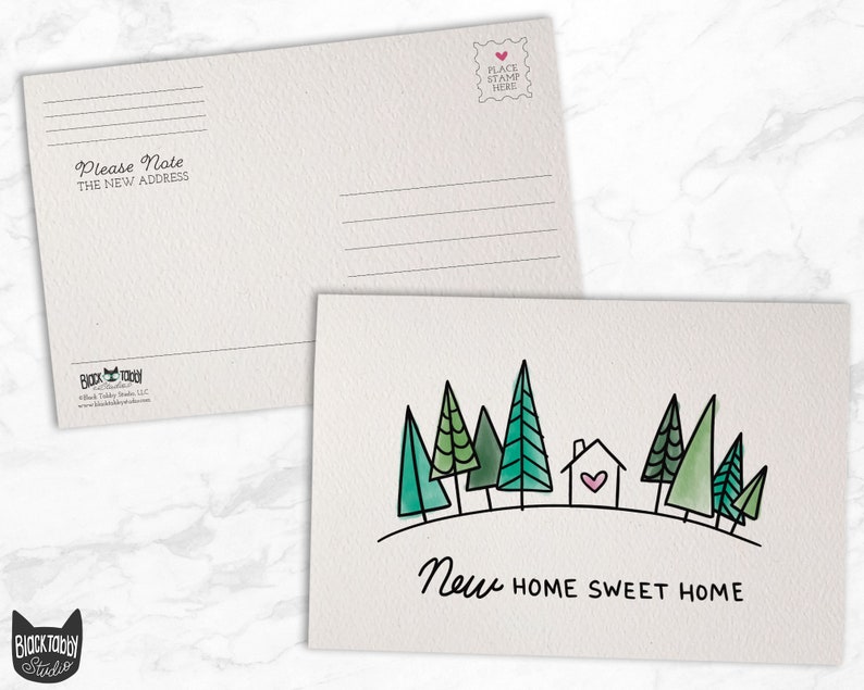 May include: A postcard with a watercolor illustration of a house with a pink heart in the window surrounded by green trees. The text "New Home Sweet Home" is written below the illustration.