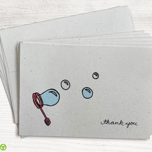 May include: A stack of thank you cards with a light gray background. The cards feature a hand-drawn illustration of a bubble wand blowing bubbles. The text "thank you" is written in black ink at the bottom of the card.