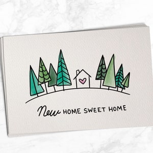 May include: A greeting card with a hand-drawn illustration of a house with a heart in the window, surrounded by green trees. The text "New Home Sweet Home" is written below the illustration.